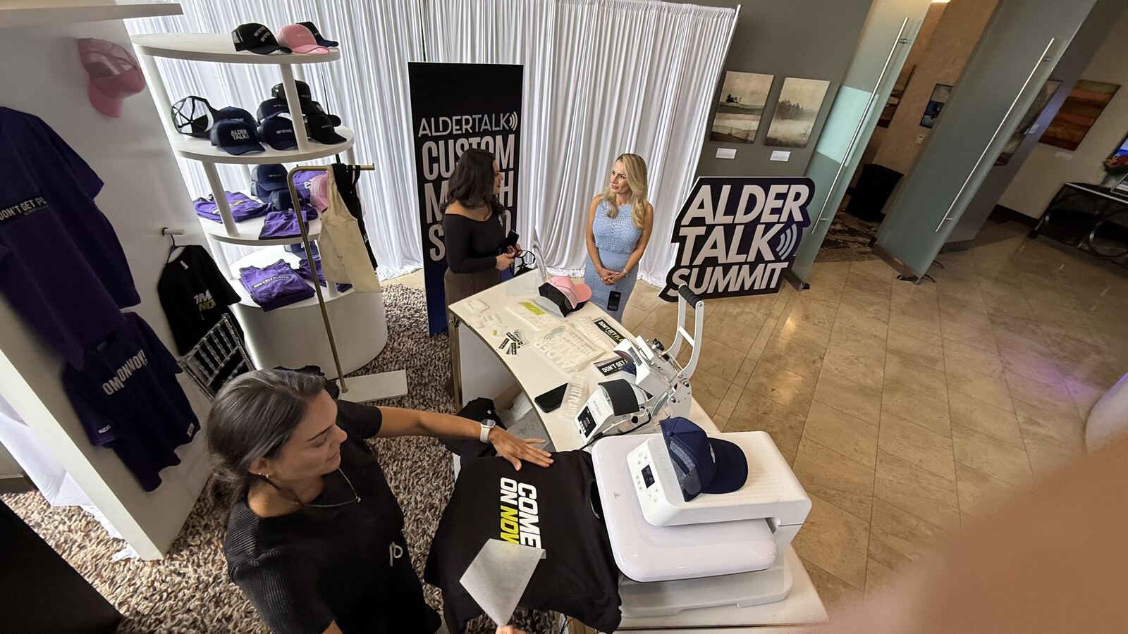 Professional Alder Talk Summit trade booth displaying branded merchandise and apparel with staff engaging with attendees